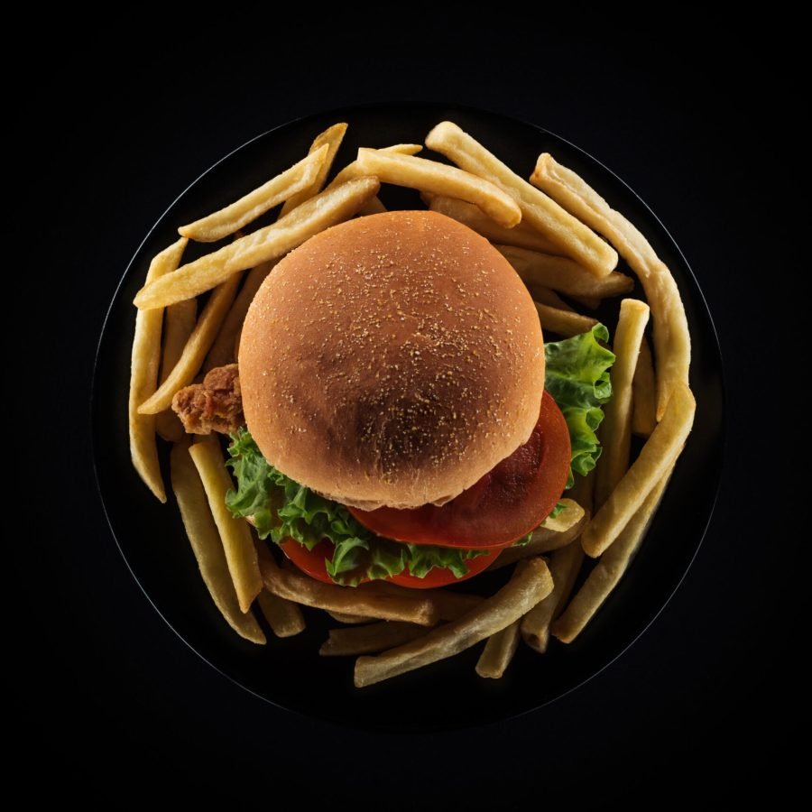 top view of tasty french fries and chicken burger on plate isolated on black